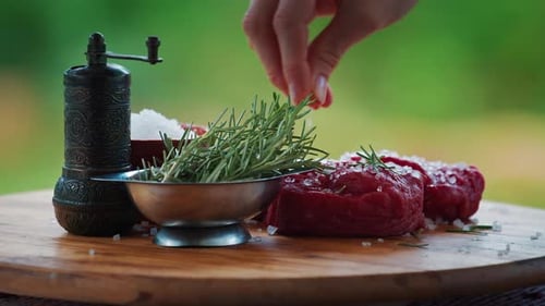 BBQ in the garden. Woman seasons filet mignon on the table with pepper and rosemary.