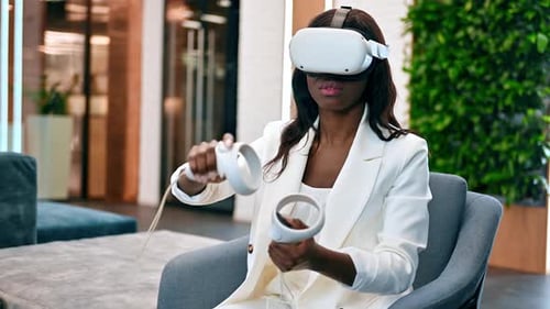 A black woman exploring virtual reality using VR glasses and controllers in an office