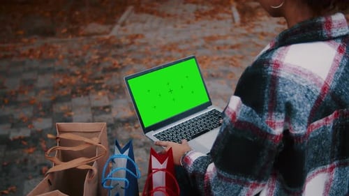 Young Woman Using Laptop with Green Screen and Shopping Bags in Autumn