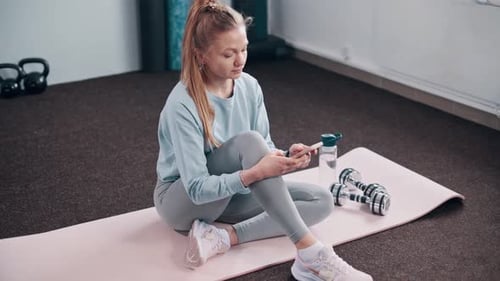 Young Woman Uses Phone After Workout Indoors