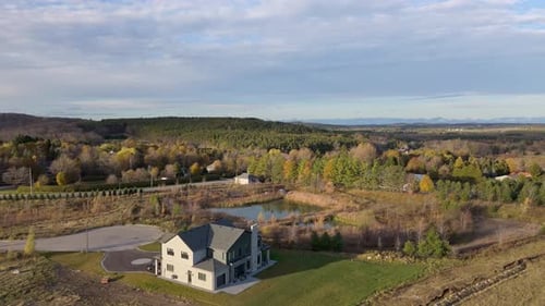 Drone shot of a newly built home surrounded by rolling hills, ponds, and autumn forest in Caledon,