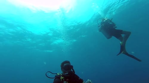 Pair of scuba divers floating just beneath the ocean surface, with one signaling to a co-diver (slow