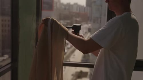 Young Adult Cleans Curtains in Urban Apartment