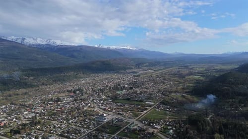 Aerial View of a Small City in a Scenic Valley Surrounded by Mountains and Green Fields