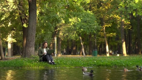 Young Woman in Glasses Working on Laptop in Riverside Park