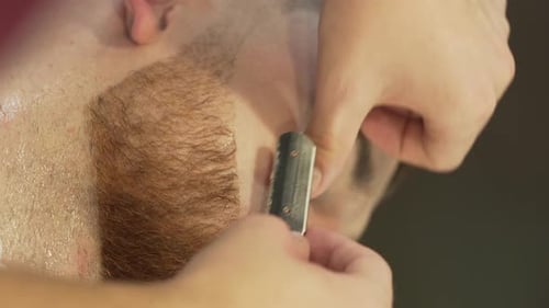 Der Friseur rasiert den Bart des Kunden sorgfältig mit einem speziellen Rasiermesser. Es ist ein Nahaufnahmevideo