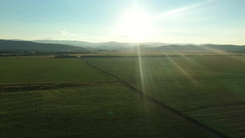 Radiant Sunlight Shining Over a Picturesque Green Field with Majestic Mountains in the Background
