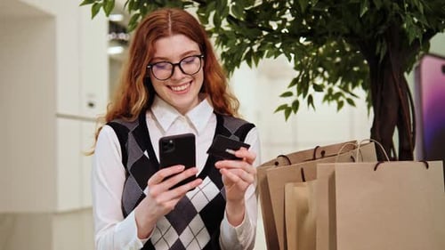 Happy Girl Credit Card in Hands Makes Online Purchases in a Shopping Center