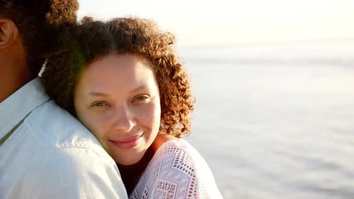 couple embraces, woman with curly hair smiling at the beach during sunset with copy space