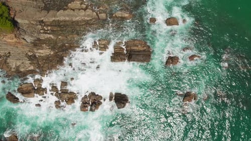 Aerial ocean waves crashing on coastal rocks in bright turquoise water