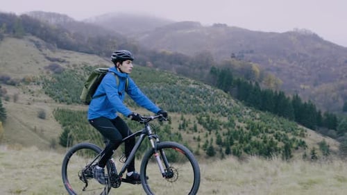 Young man cycling through beautiful autumn nature on a hilly forest trail