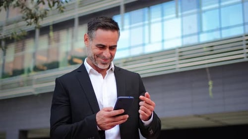 Smiling Man in Suit Using Smartphone Outside Office