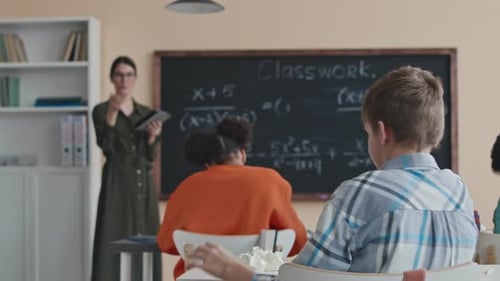 Student Solving Math Problem on Chalkboard with Teacher