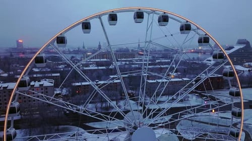 Large Ferris Wheel Overlooking Winter City Skyline During Cold Dusk