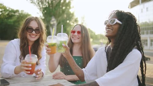 Three young women toasting colorful drinks at table
