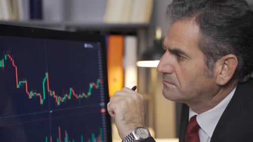 Professional mature man doing stock market and cryptocurrency investment analysis from computer.