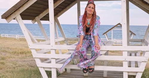 Portrait of Smiling Woman with Dreadlocks in Boho Style in Rustic Wooden Gazebo on the Sea
