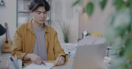 Young Adult Works and Talks on Phone at Desk