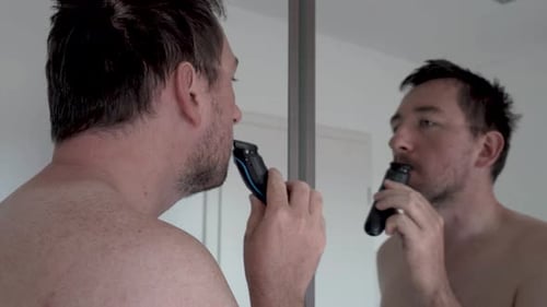 Man shaving his beard in front of a mirror with an electrical razor