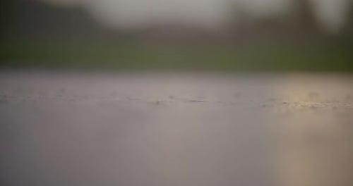 Rain Falling on Wet Glass with Blurred Green Background and Reflective Water Below