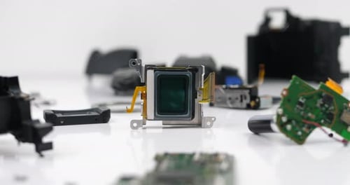 Closeup of disassembled camera sensor and broken camera parts on the desk in workshop. Broken camera