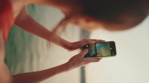 Close-up, girl stand on the embankment and takes pictures of sunrise on mobile phone