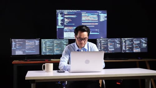 Programmer Walking Into The Working Space To Write Code By A Laptop Using Multiple Monitors