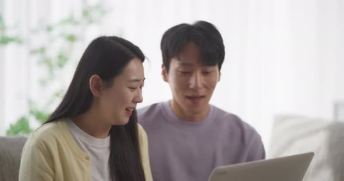 Young Adults Using Laptop Together Indoors on Couch