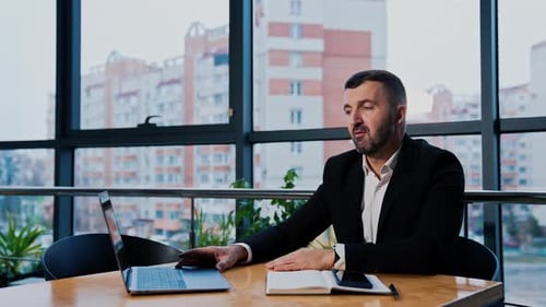 Confident mid-aged businessman works on his laptop in office.