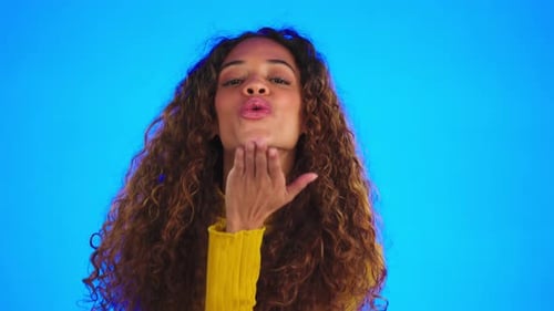 Face, flirt and happy woman blowing kiss in studio, beautiful and confident on blue background