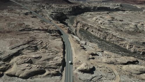 A solitary camper truck winds its way along the road, traversing the desolate landscapes of Utah, US