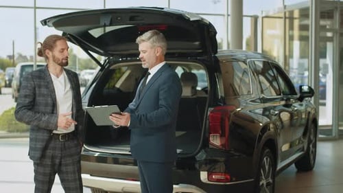 Happy Car Salesman and Male Customer in Auto Dealership They are Shaking Hands
