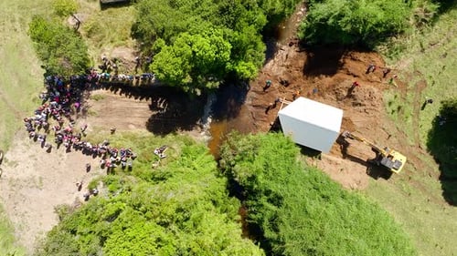 Aerial Bird’s-Eye View of an Excavator Positioning a House Near River Crossing in Chiloé, Chile.