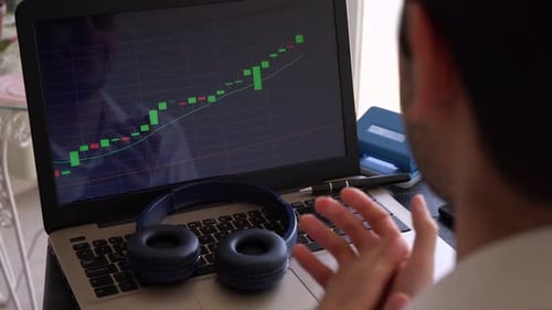 Man Watches Stock Chart on Laptop, Pumps Fist