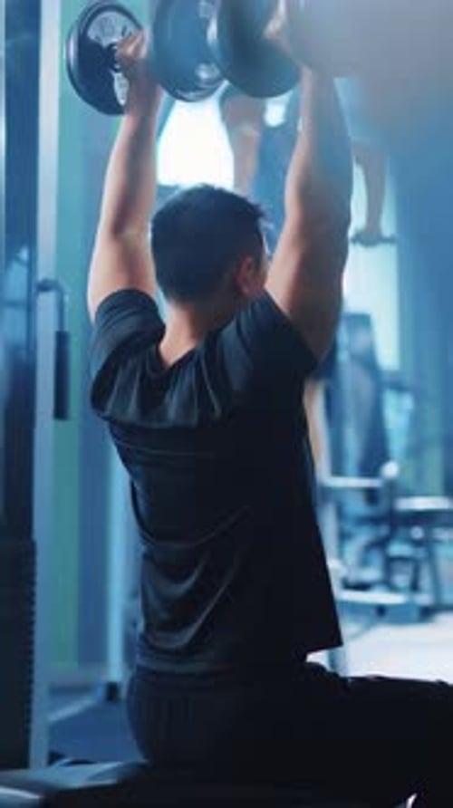 Un hombre levanta mancuernas en un gimnasio y se concentra en el entrenamiento de fuerza para desarrollar músculo