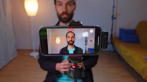 A Young Bloger Records a Video with Himself on Smartphone in His Room Studio