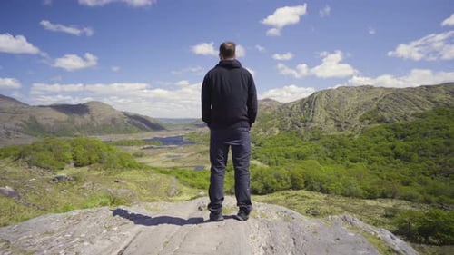 Dolly forward shot of a person standing on the edge of a rock with epic landscapes with wonderful sk