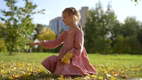 Happy Little Girl Sitting and Playing with Fallen Leaves in Autumn Park Fall Season