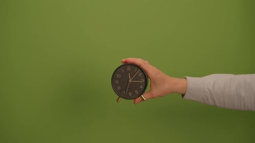 A Hand Gracefully Holding a Clock Set Against a Bright and Vibrant Green Background