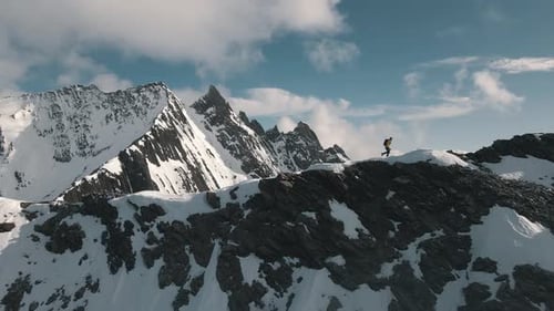Mountaineer walks along the ridge to a summit. In the background a prominent mountain partly covered