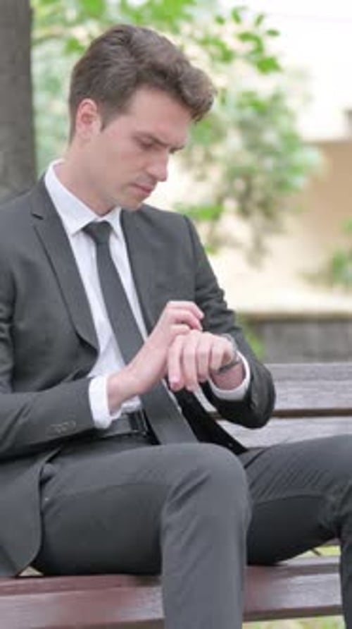 Man in Suit Checking Watch While Sitting on Bench