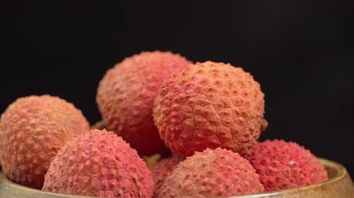 Frische Litschifrüchte in der Schale rotieren in einer Holzschale im Makro auf schwarzem Hintergrund. Litschibeeren