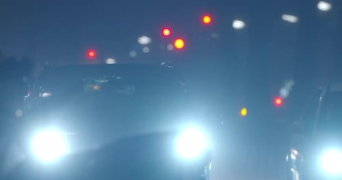 Car with dazzle lights moving slowly in night city under the rain