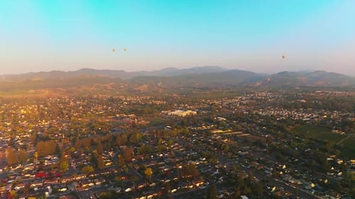 Hot air balloons flying over the beautiful city. Sunlit scenery of Napa, California, USA