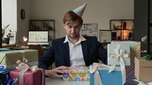 Excited Man Opens Birthday Gifts at Office Desk