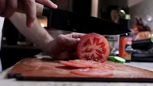 Male Caucasian hand slicing red raw tomato on chopping block with sharp knife, static side close up