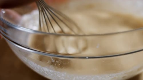 Macro View of Mixing Fresh Eggs Flour and Milk with Steel Hand Mixer in a Glass Bowl