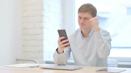 Young Man Celebrates Success on Mobile Phone