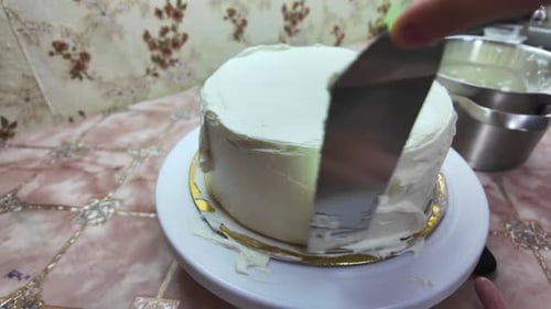 Applying white frosting to a festive cake. Kitchen utensils and a bowl of frosting nearby.