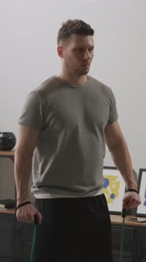 Focused Man Performing Resistance Band Shoulder Workout at Home Raising Arms to the Sides to Build